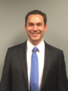 CenYing學術總監Daniel Eyrich身穿西裝與藍色領帶，面帶微笑站在灰色背景前。